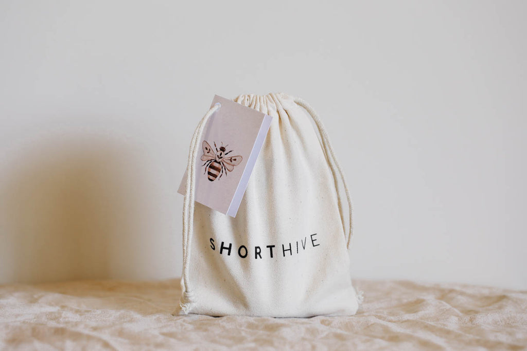 ShortHive infused honey calico bag with bee gift tag. Pictured on white background